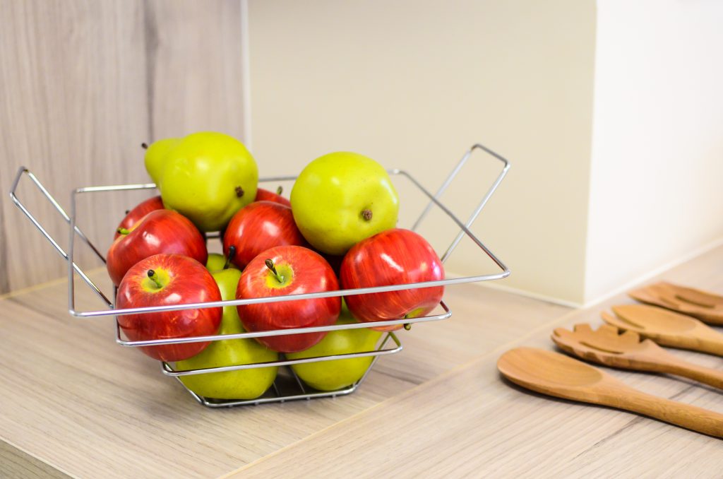 Em uma mesa, uma fruteira com maças vermelhas e verdes.