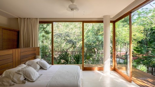 Imagem de um quarto com uma cama de casal, onde as janelas são de madeira 